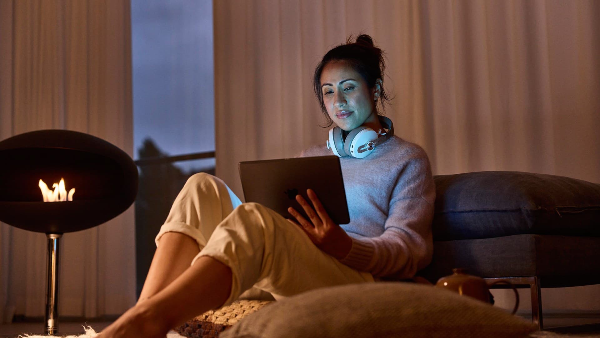 Symbolbild: Eine Frau auf einem Sofa hält einen Tabletcomputer, mit dem man Smart Home Funktionen steuern kann.