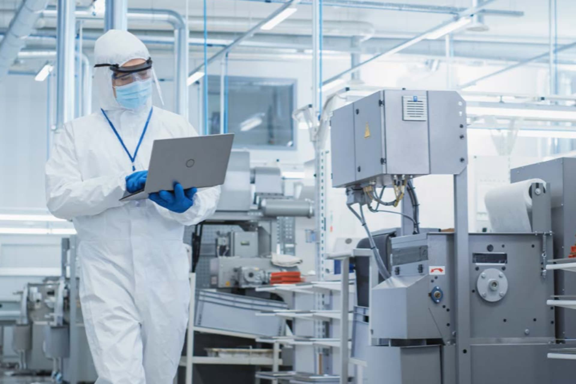 Ein Techniker überwacht in Schutzkleidung die Produktionsanlage und prüft Prozessdaten direkt am Laptop – für sichere, präzise und hygienisch einwandfreie Abläufe in der Life-Science-Fertigung.