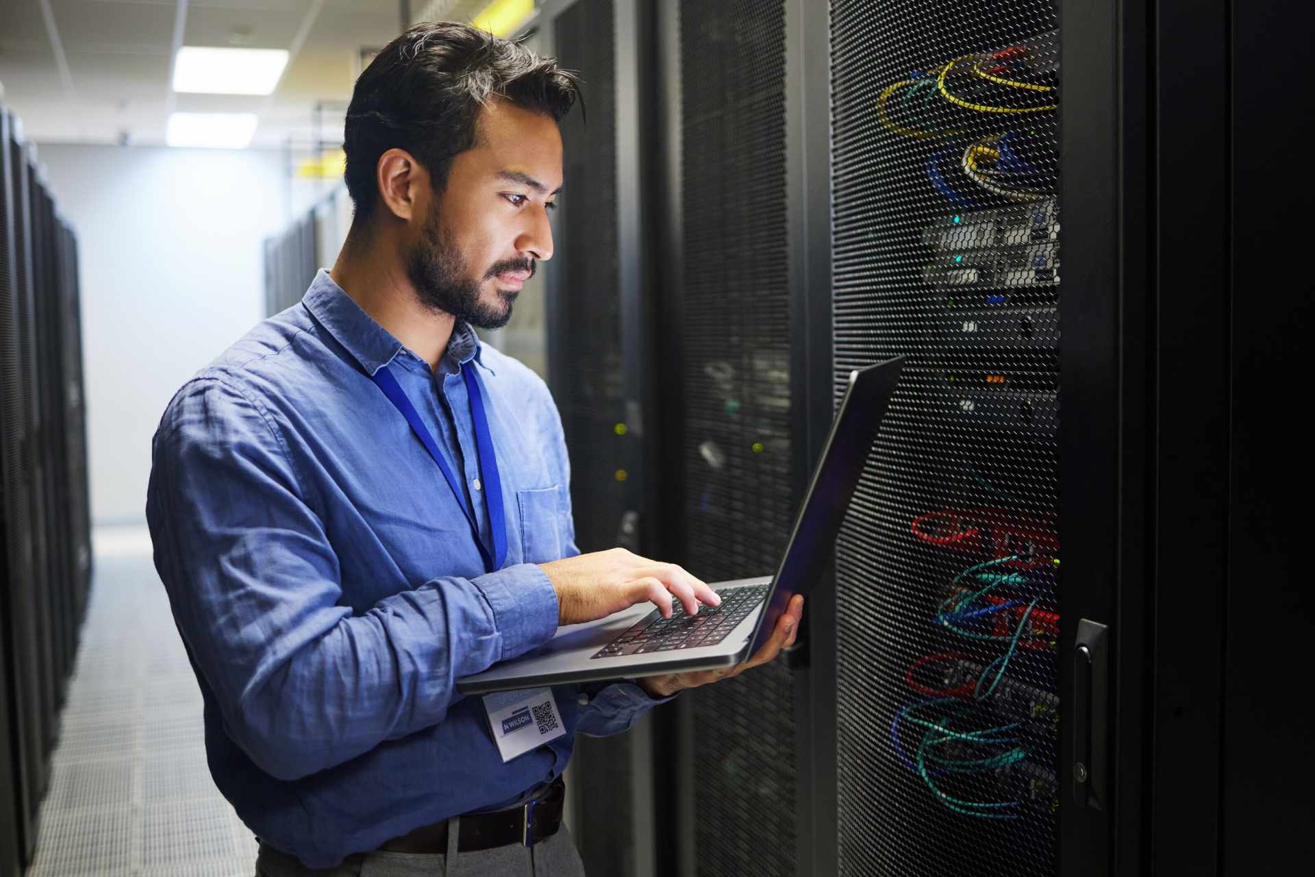 Mann steht vor Serverschrank mit Laptop-Header